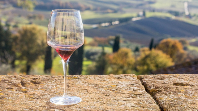 Glass of red wine on a ledge overlooking the rolling landscape of Tuscany